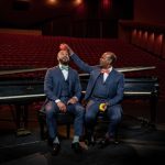 Barron and Donald Ryan sit playfully in front of two grand pianos.