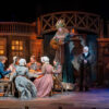 The Cratchit family enjoys Christmas dinner, while Scrooge and the Ghost of Christmas Present look on. • The cast of KCRep's 2023 production of A CHRISTMAS CAROL • Photo by Don Ipock