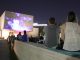 In the foreground two people attend a concert on the lawn of Nerman Museum. Images are displayed on the exterior wall of the museum.